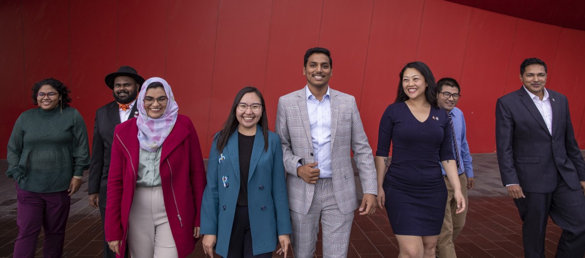 Six Scholar Champions standing together against a red wall
